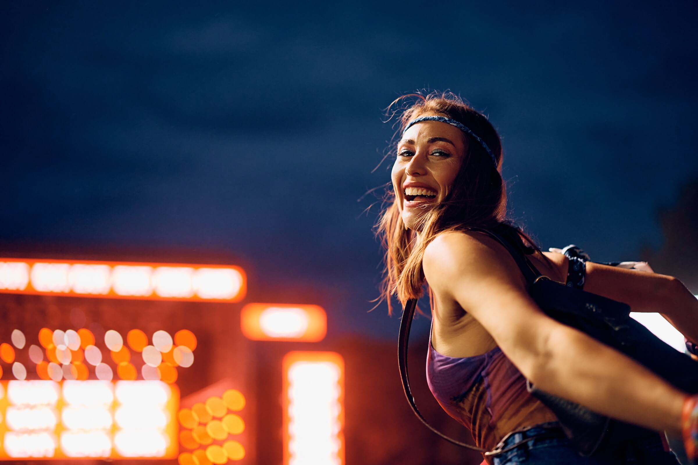 Szczęśliwa kobieta dobrze się bawi podczas wieczornego koncertu muzycznego na świeżym powietrzu i patrzy w kamerę